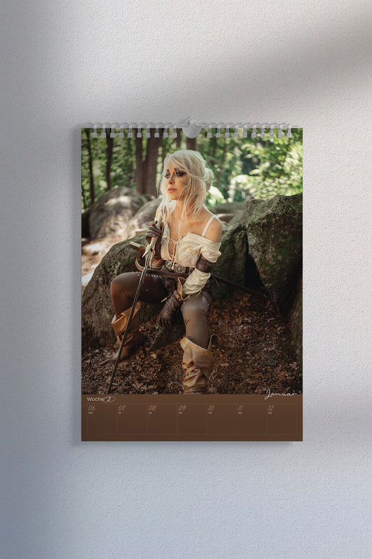 Kalenderseite mit Cosplay-Foto einer Kämpferin mit weißblonder Perücke und Schwert, sitzend in einem bewaldeten Natur-Setting. Unten der Wochenplaner „Januar, Woche 2“.