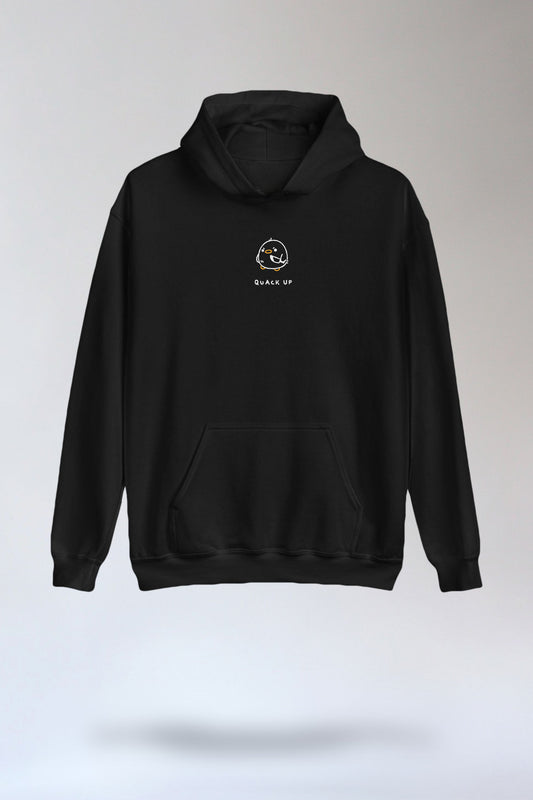 Schwarzer Kapuzenpullover mit Kängurutasche und kleinem Frontprint mittig auf der Brust. Das Motiv zeigt ein minimalistisches, rundes Entengesicht mit orangefarbenem Schnabel und Füßen, ergänzt durch den Schriftzug „QUACK UP“ in weißen Großbuchstaben darunter.