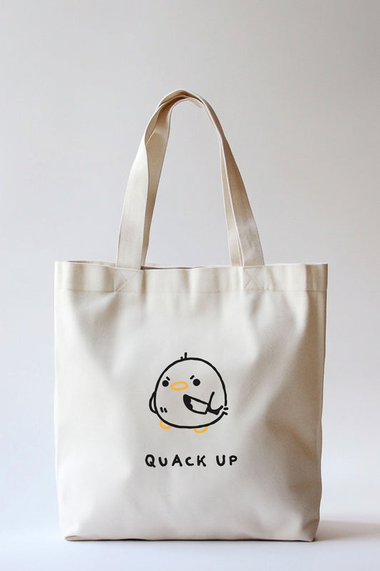 Naturfarbene Stofftragetasche mit zwei Henkeln, mittig bedruckt mit einer stilisierten, schwarzen Zeichnung eines runden Entenkükens mit orangefarbenem Schnabel und Füßen. Die Ente hält ein kleines Messer in der Hand. Darunter der schwarze Schriftzug: „QUACK UP“.
