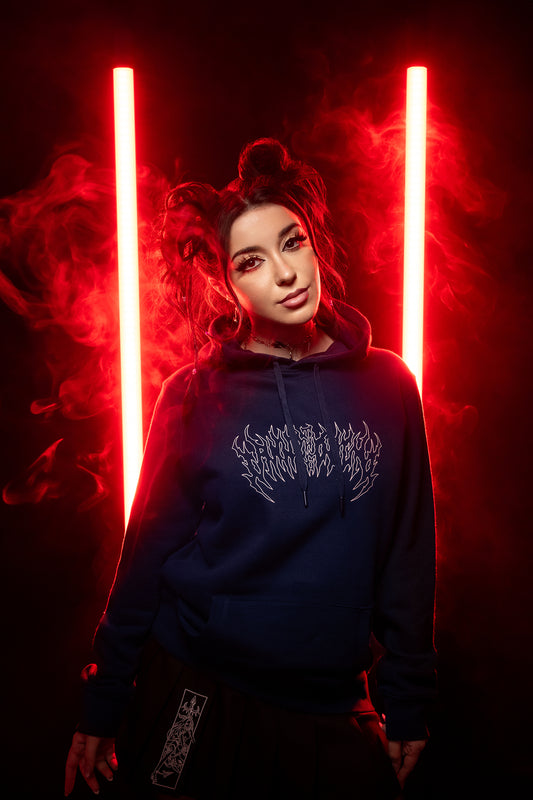 Studioaufnahme mit rotem Licht und Nebel: Person trägt den dunkelblauen Hoodie mit weißem Frontprint, kombiniert mit schwarzem Faltenrock und sichtbarem Patch auf dem Rocksaum.