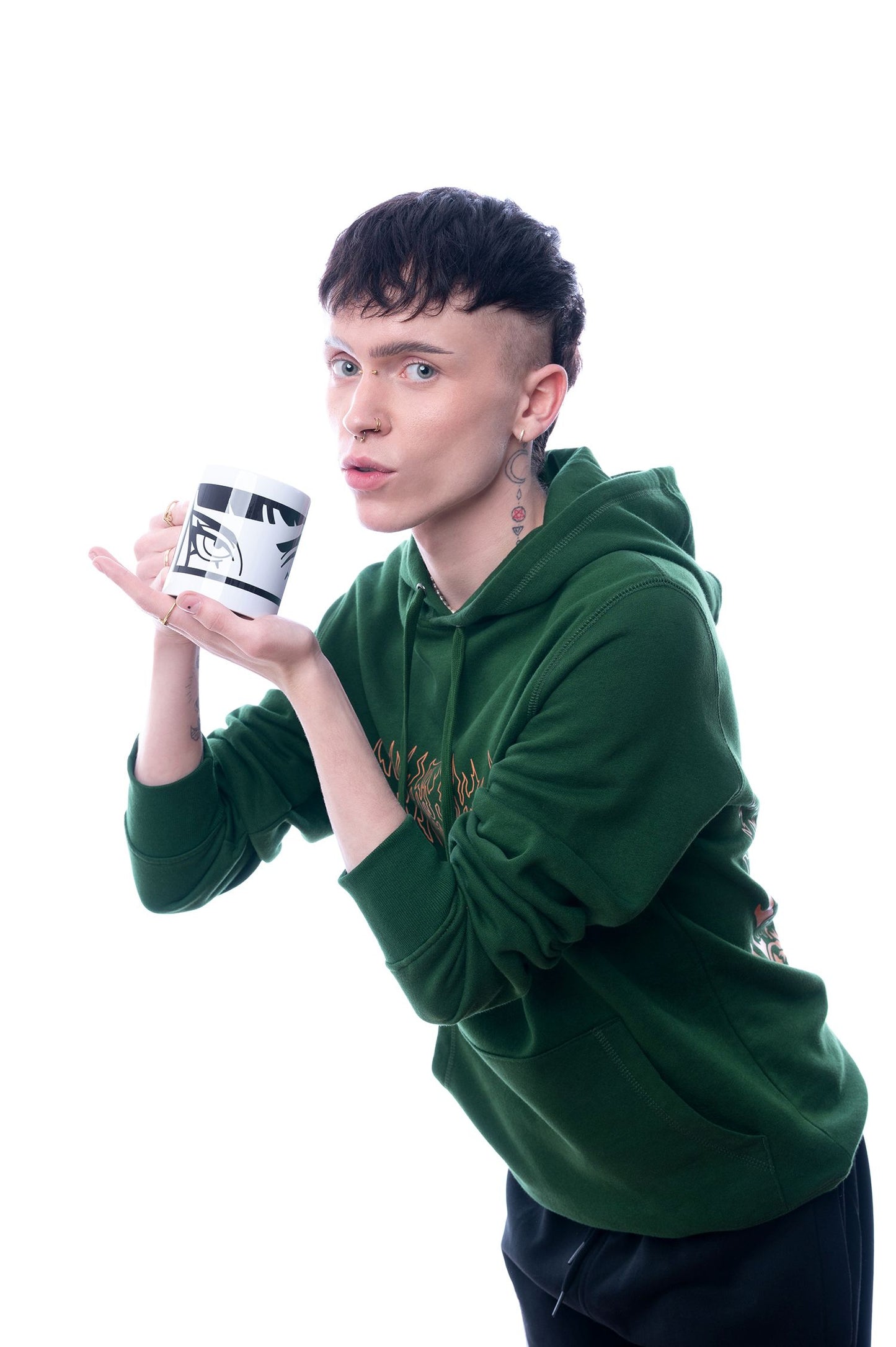 Weiße Tasse mit grafischem, schwarzem Augenmotiv. Die Tasse wird auf eine verspielte Weise in Szene gesetzt und mit einer präsentierenden Handgeste hervorgehoben.