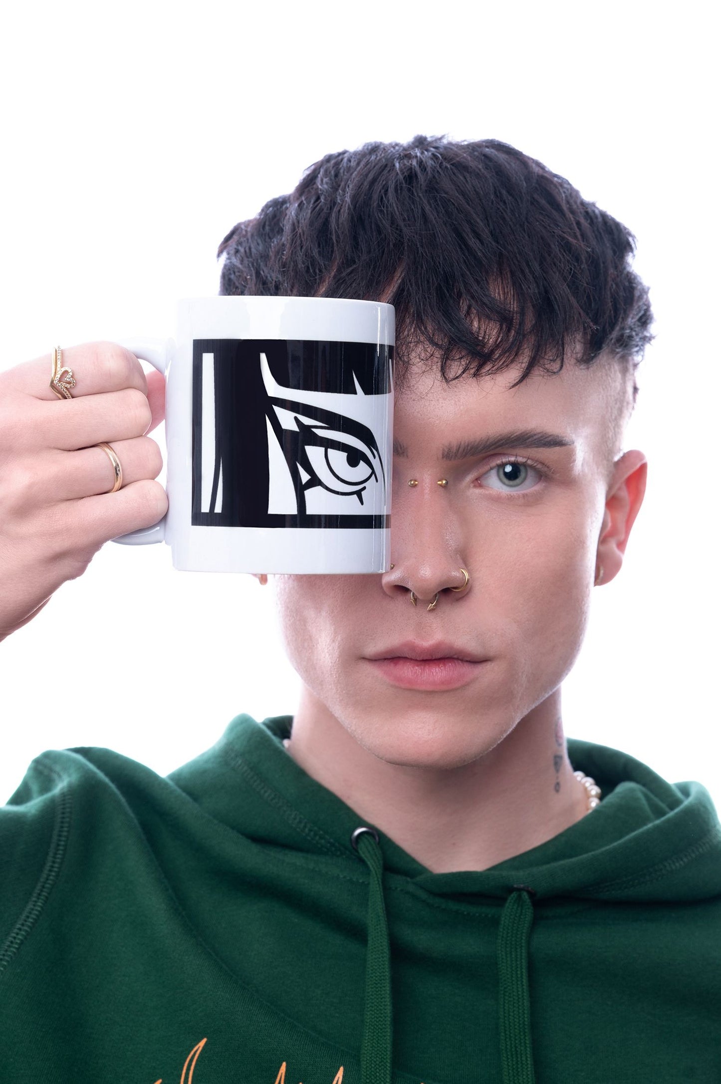 Weiße Tasse mit schwarzem Augenmotiv wird direkt vor das Gesicht gehalten, sodass das aufgedruckte Auge perfekt mit dem echten Auge der Person übereinstimmt.