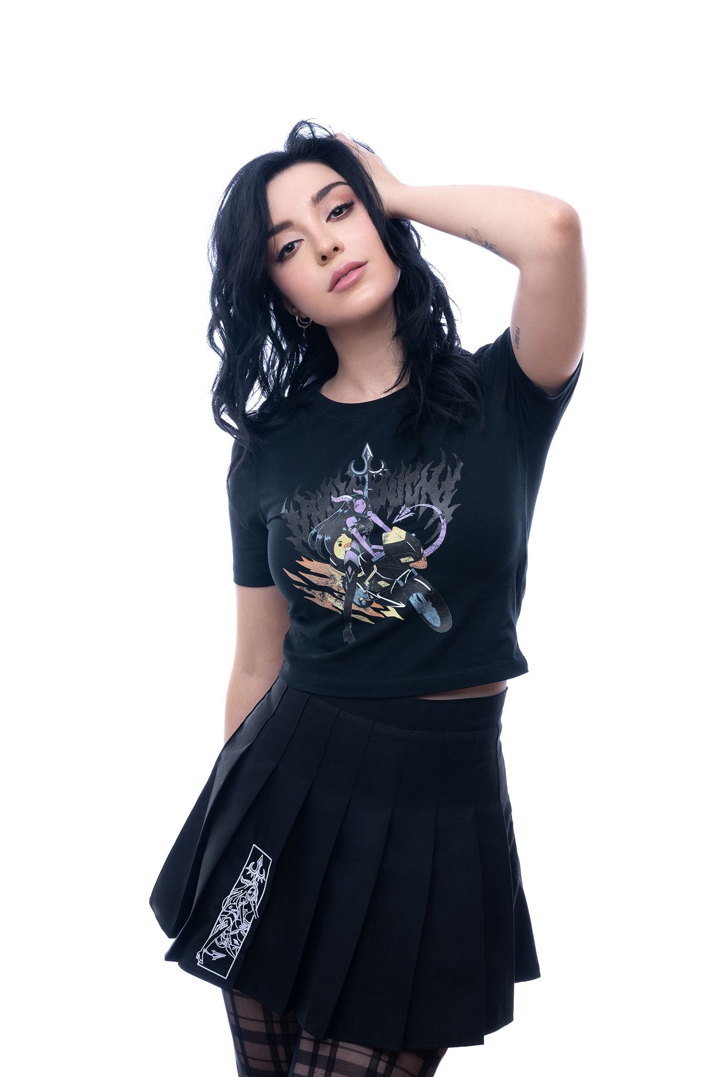 Schwarzes T-Shirt mit mehrfarbigem Print einer Dämonin auf Motorrad, kombiniert mit schwarzem Rock; Model posiert mit Hand am Kopf, Blick in die Kamera.