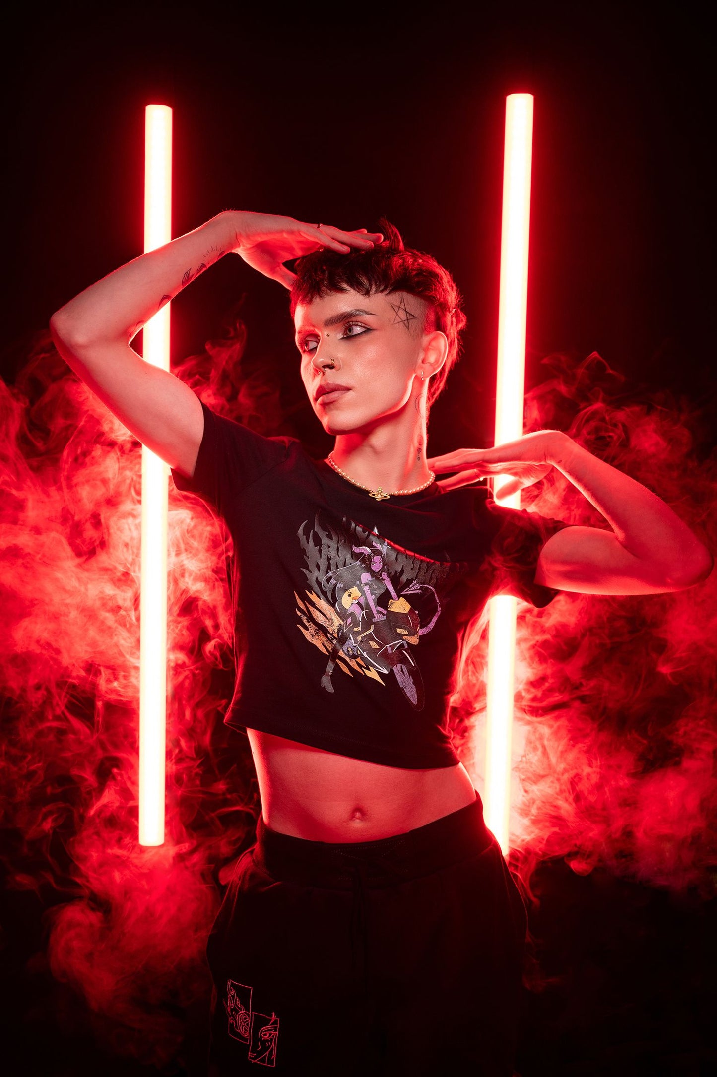 T-Shirt mit farbigem Dämoninnenmotiv, kombiniert mit schwarzem Rock, fotografiert im roten Licht mit Studioeffekten; Model posiert seitlich.