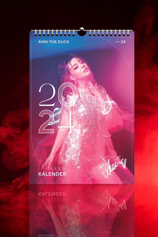 Cover des „Anni the Duck Moods“-Kalenders 2024, zeigt Anni in silbernem Fransen-Kleid mit weichem Lichtverlauf in Pink, Violett und Blau. Weißer Schriftzug „2024“ und Autogramm unten.