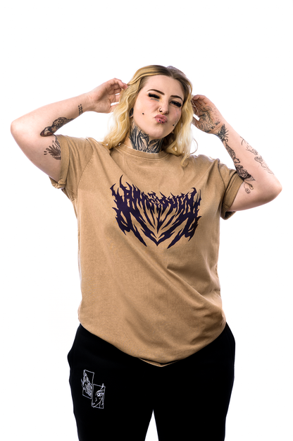 	Braunes T-Shirt mit violettem Flammenschriftzug auf der Vorderseite, getragen von einer tätowierten Person, die mit gekreuzten Armen und Kussmund posiert.
