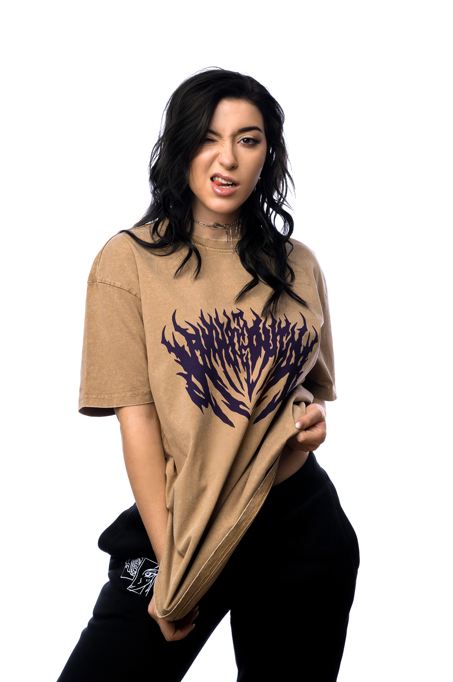 Person zwinkert frech in die Kamera und zieht am braunen T-Shirt mit violettem Frontprint im Flammendesign.