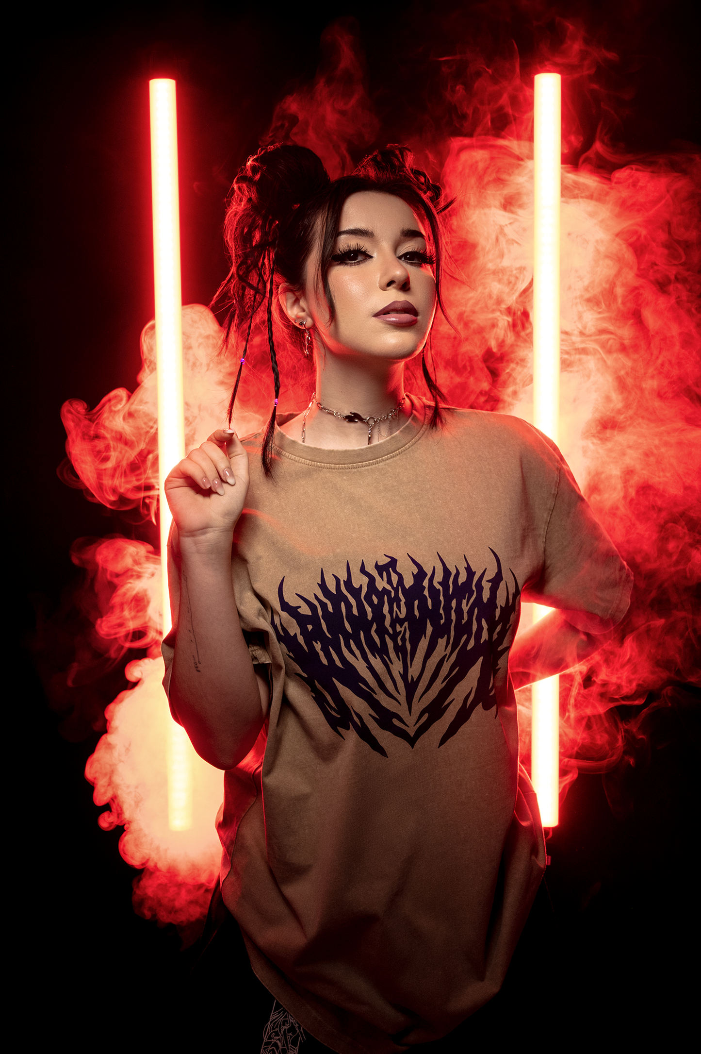 Das braune T-Shirt mit Flammenprint wird vor rot leuchtendem Hintergrund von einer Person mit Zöpfen getragen.