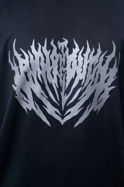 Nahaufnahme eines schwarzen T-Shirts mit großem silbergrauen Print auf der Brust. Der Druck zeigt ein symmetrisch ausgerichtetes, stilisiertes Flammenmuster mit spitz zulaufenden Formen.