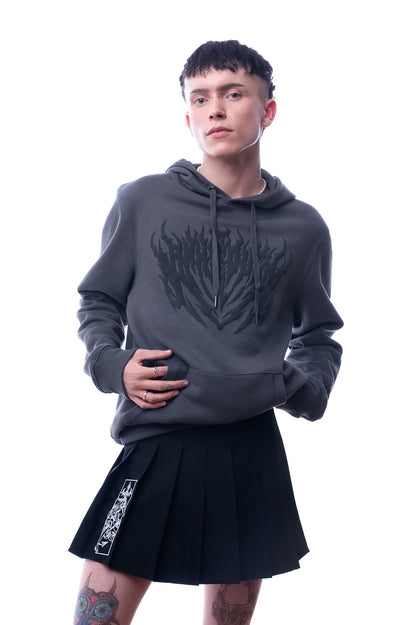 Dunkelgrauer Hoodie mit schwarzem Flammenprint auf der Vorderseite. Die Person trägt dazu einen schwarzen Faltenrock mit weißem grafischen Print auf dem linken Bein. Studioaufnahme mit Blick auf das ganze Oberteil.