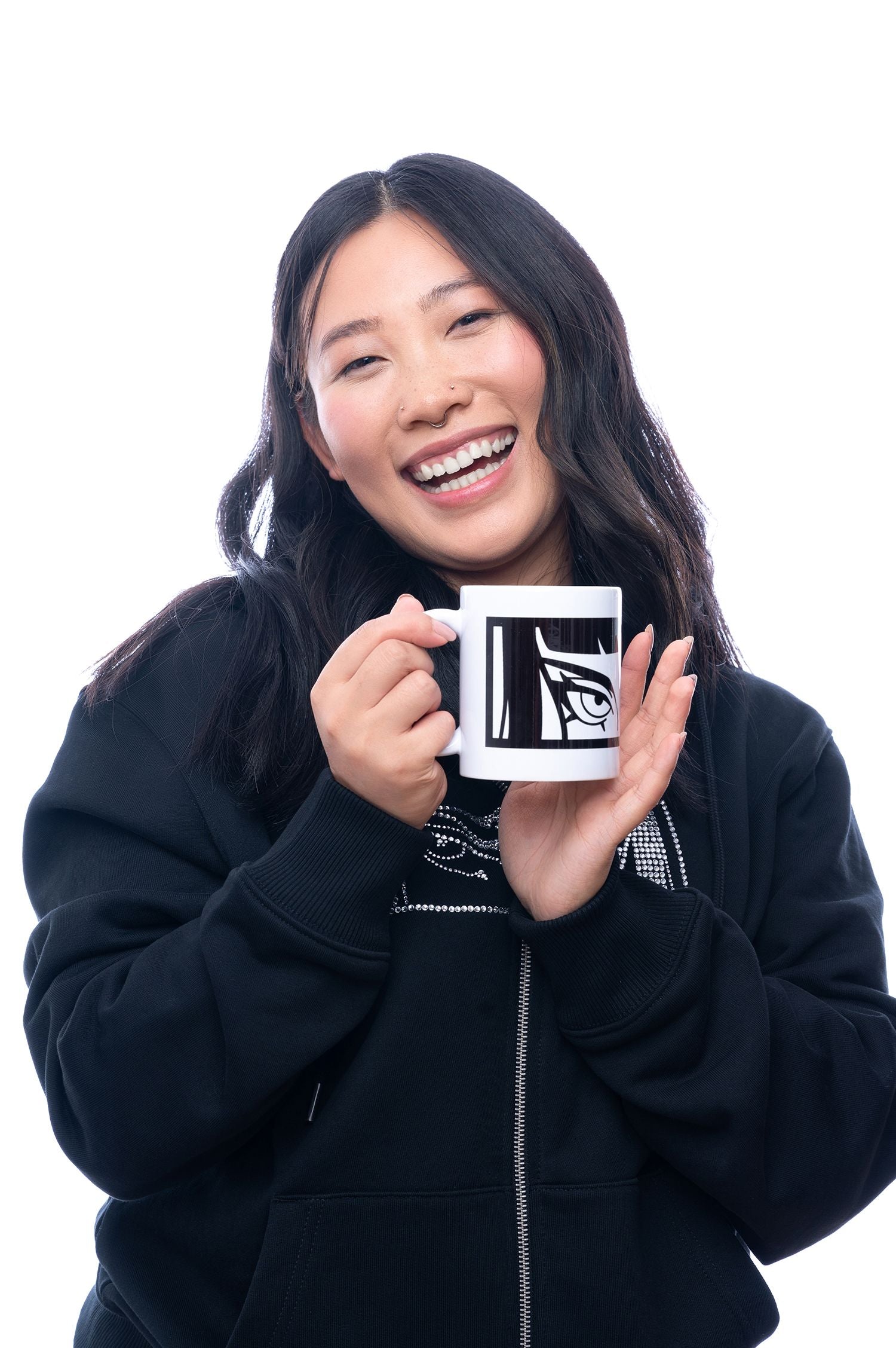 „Weiße Tasse mit schwarzem, stilisiertem Augenmotiv auf der Vorderseite. Die Tasse wird von einer lachenden Person mit beiden Händen präsentiert.“