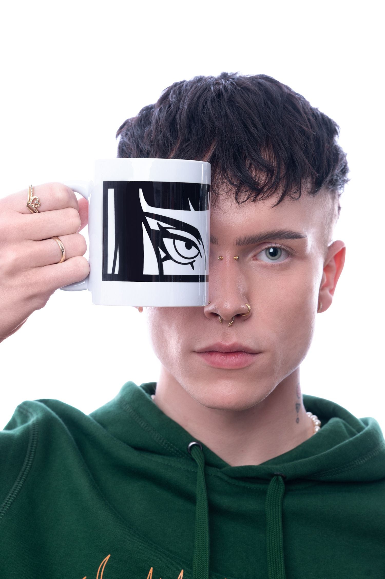 Weiße Tasse mit schwarzem Augenmotiv wird direkt vor das Gesicht gehalten, sodass das aufgedruckte Auge perfekt mit dem echten Auge der Person übereinstimmt.